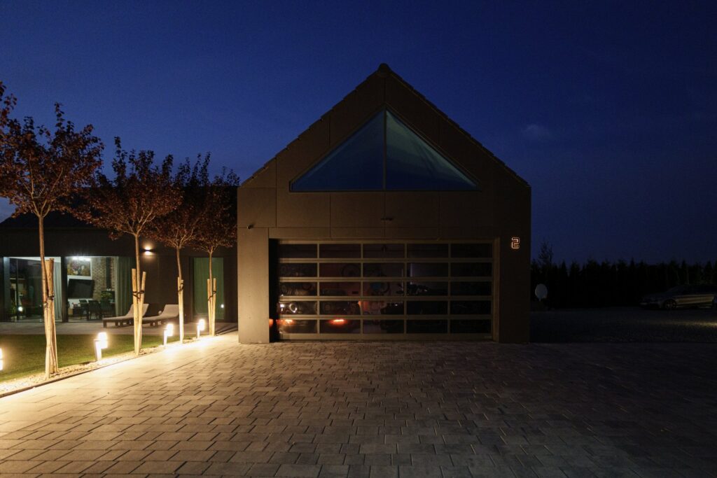 Oświetlenie podjazdu i wejścia do nowoczesnego domu z lampami liniowymi przy drzewach